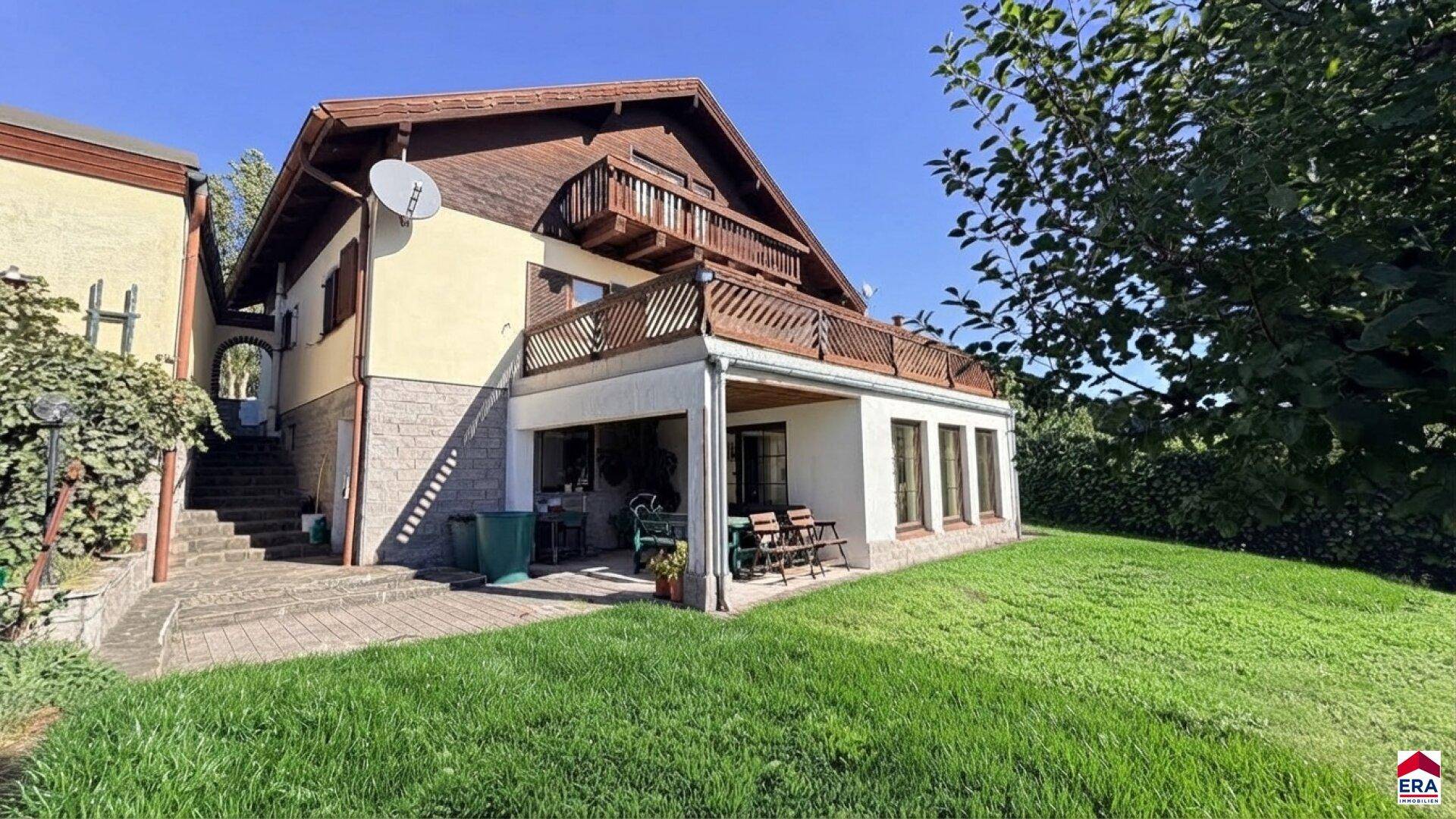 Seitenansicht des Hauses mit Garten, gepflastertem Bereich und Außentreppe.