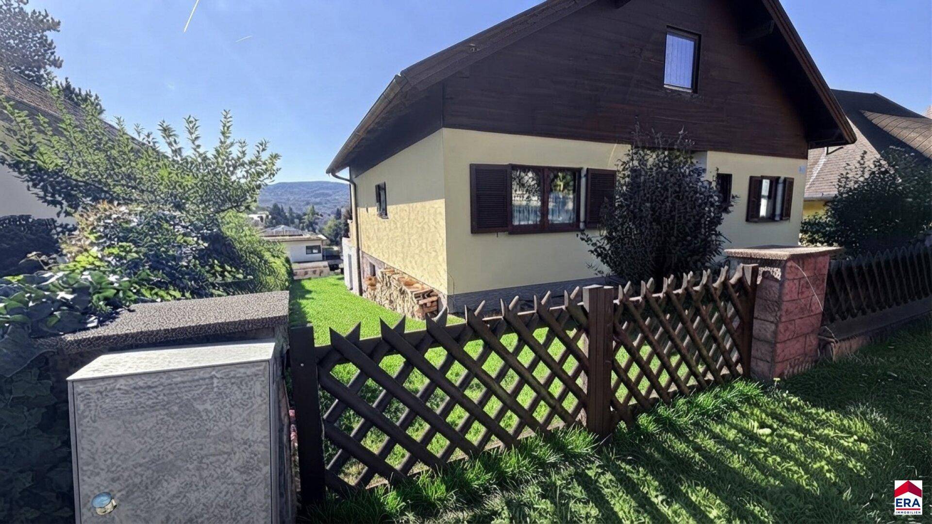 Seitenansicht des Hauses mit Holzzaun und Blick auf die Umgebung.