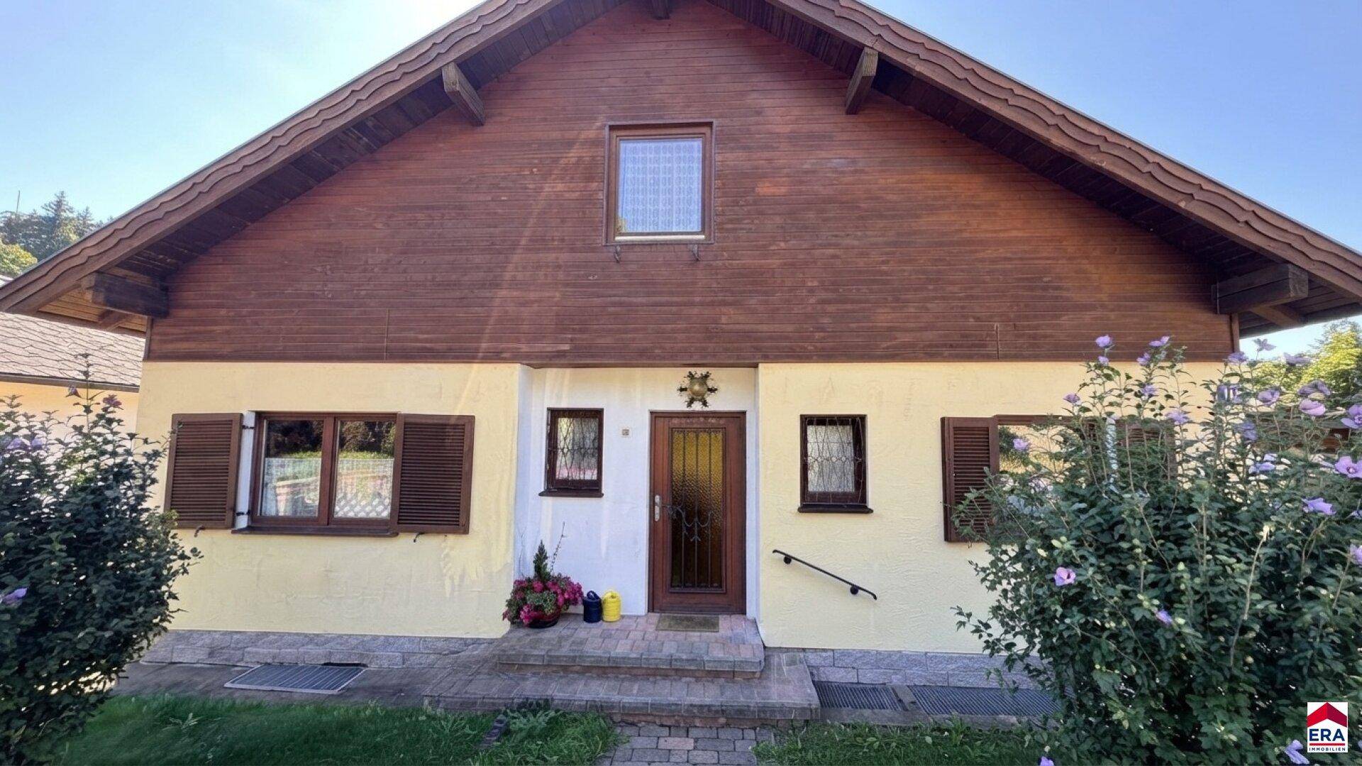 Frontansicht des Hauses mit Holztür, Fensterläden und gepflegter Bepflanzung.