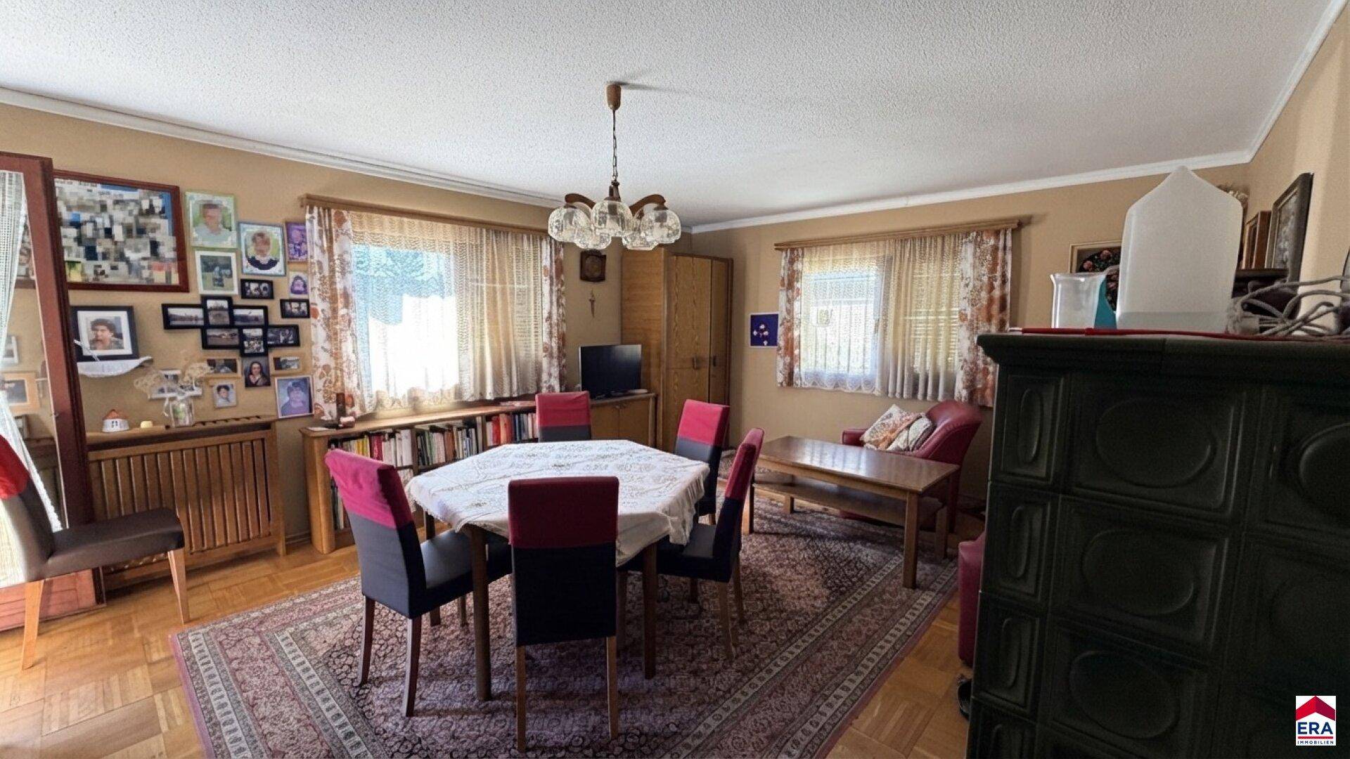 Gemütlicher Wohn-Essbereich mit traditionellem Kachelofen, Holzboden und Teppich.