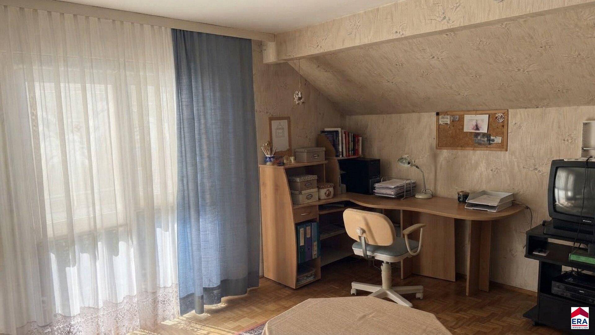 Helles Arbeitszimmer im Dachgeschoss mit Schreibtisch, Bücherregal und Fenster.