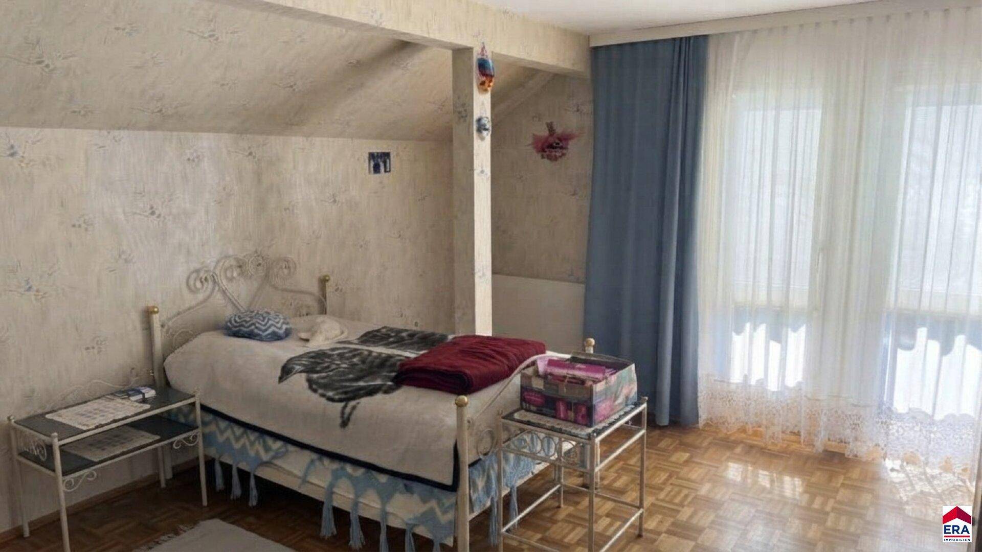 Schlafzimmer im Dachgeschoss mit Einzelbett, Holzboden und großen Fenstern.