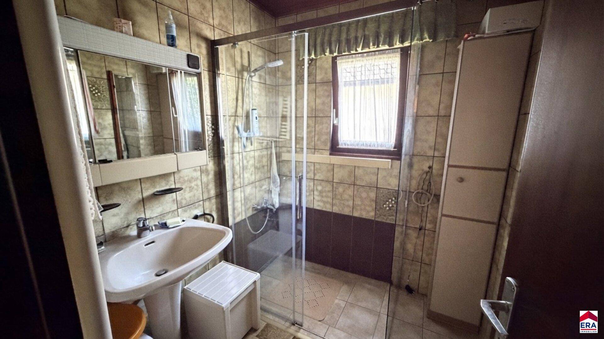 Badezimmer mit Duschkabine, Waschbecken und braunen Fliesen im 80er-Jahre-Stil.