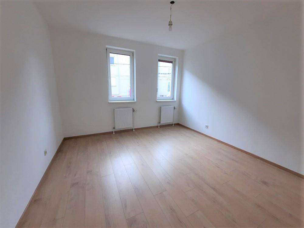Helles Schlafzimmer mit Laminatboden und zwei Fenstern für gute Belichtung.