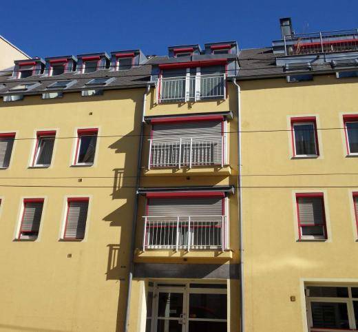 Gelbe Fassade eines Mehrfamilienhauses mit mehreren Balkonen und Rollläden.