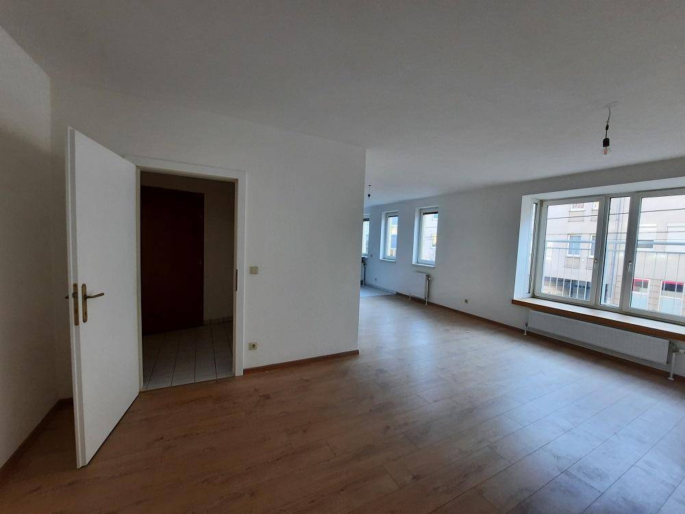 Großer Wohnraum mit Laminatboden und Fenstern, die viel Tageslicht hereinlassen.