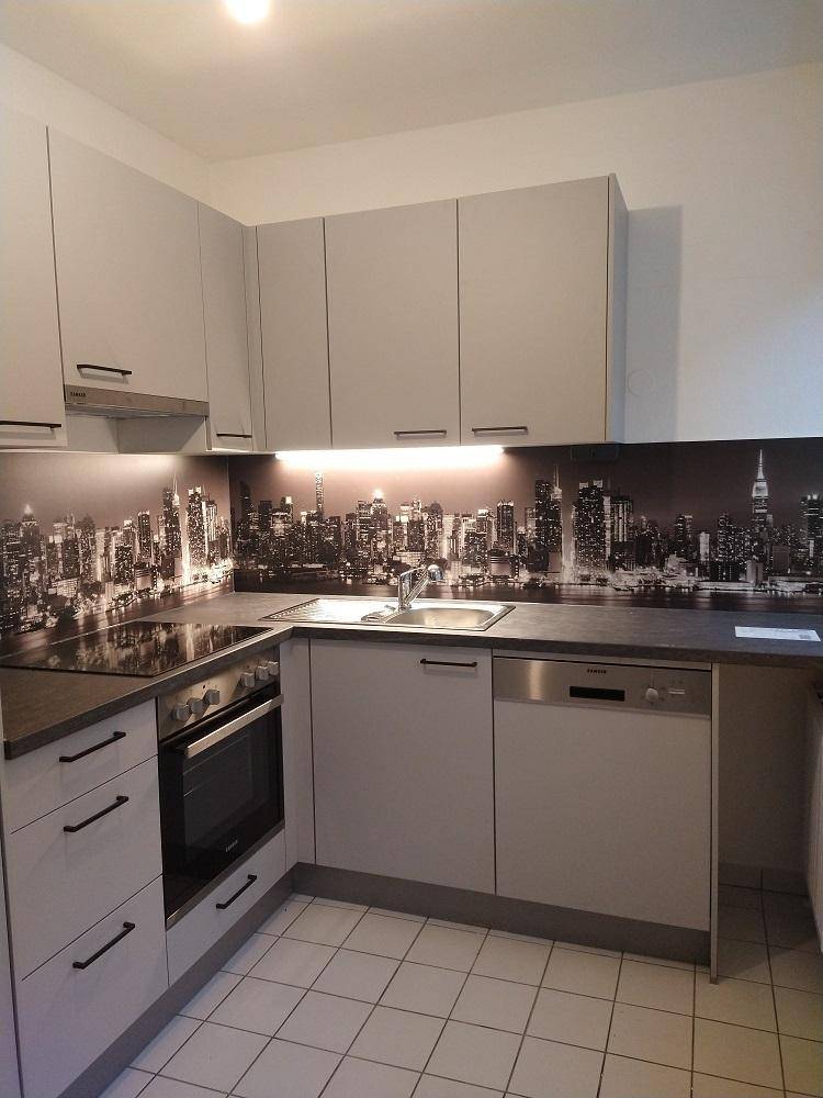 Helle Einbauküche mit grauen Schränken, integrierten Geräten und einer stilvollen Skyline-Rückwand.