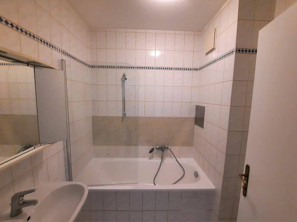 Badezimmer mit Badewanne, Fliesenboden und einem Spiegel über dem Waschbecken.