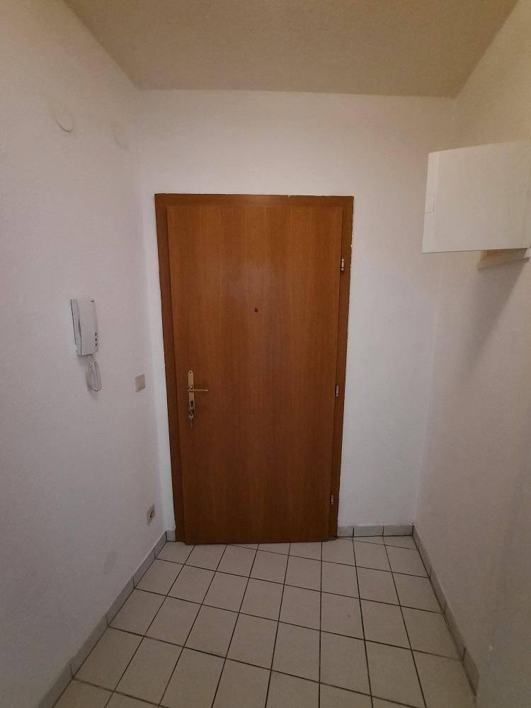Eingangsbereich mit Fliesenboden und einer Holztür, die in die Wohnung führt.