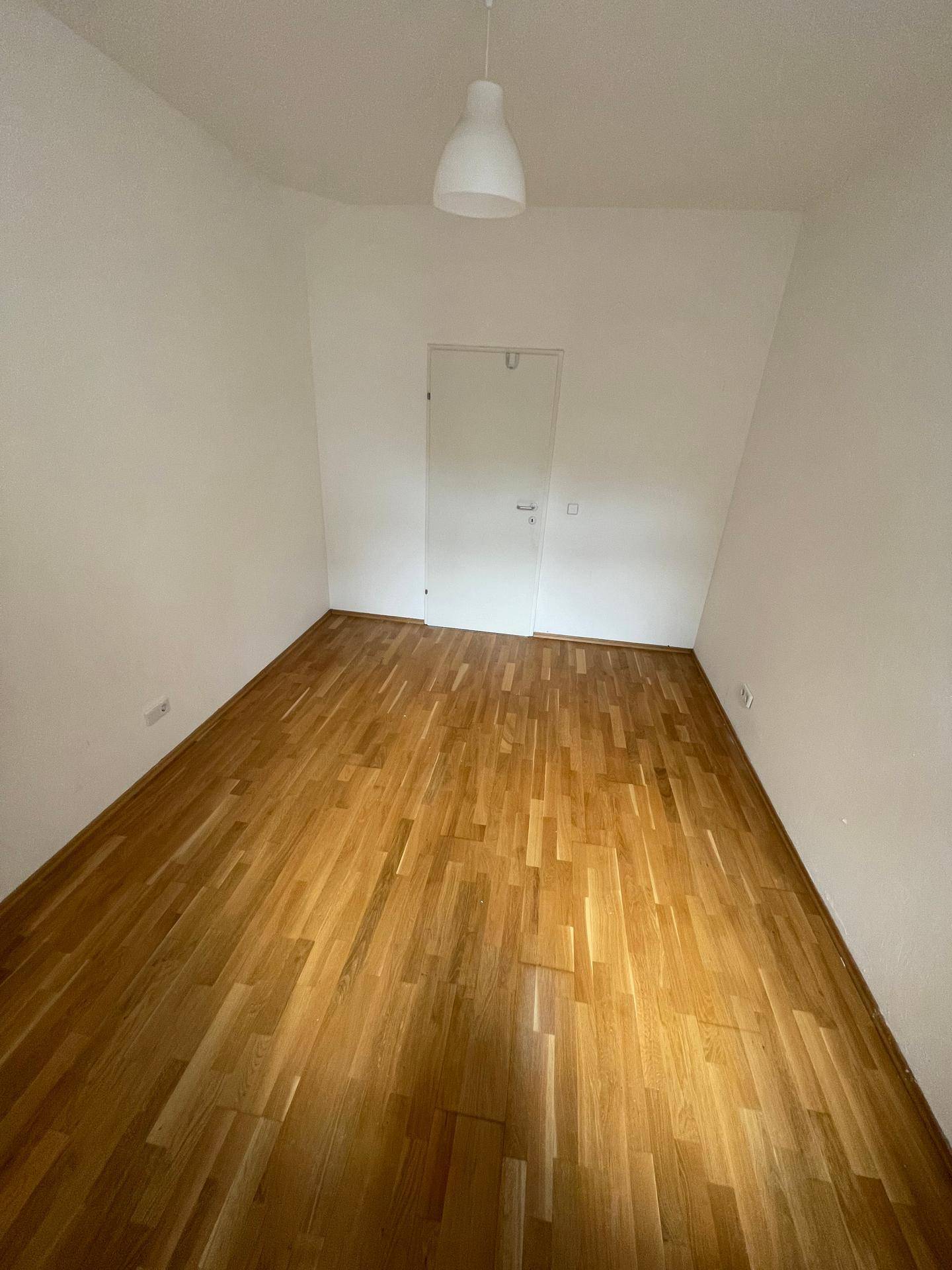 Leeres Zimmer mit Holzboden und weiß gestrichenen Wänden, bereit zum Einzug.