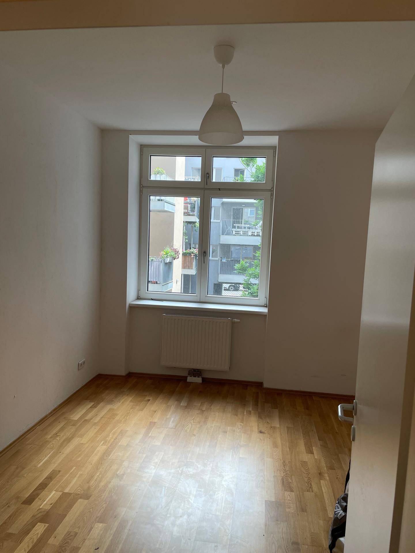 Helles Zimmer mit Holzboden und großem Fenster, ideal als Schlaf- oder Arbeitszimmer.