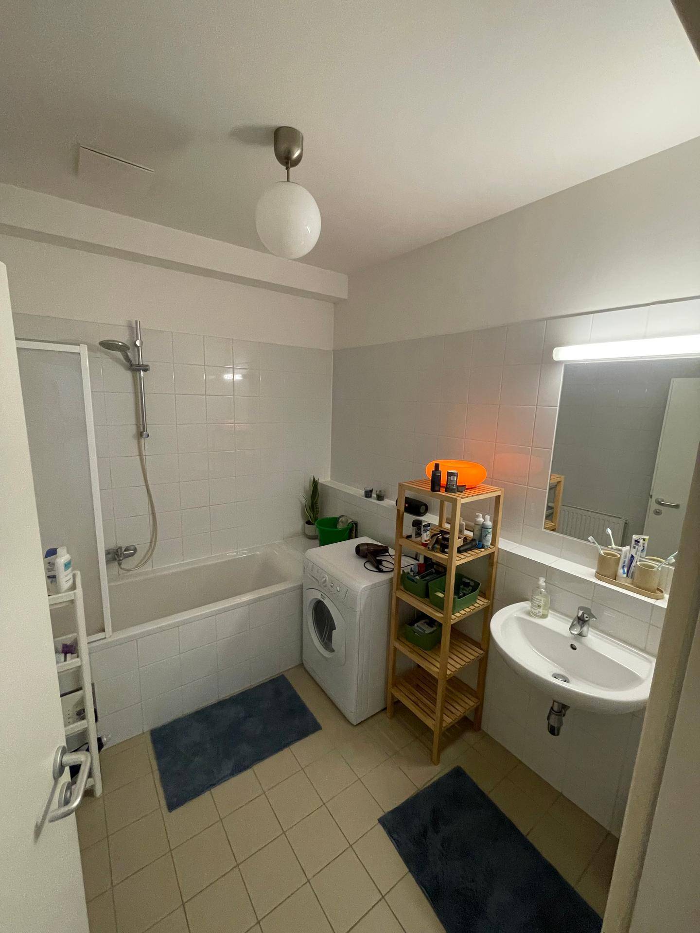 Badezimmer mit Badewanne, Waschbecken, Waschmaschine und hellen Fliesen.