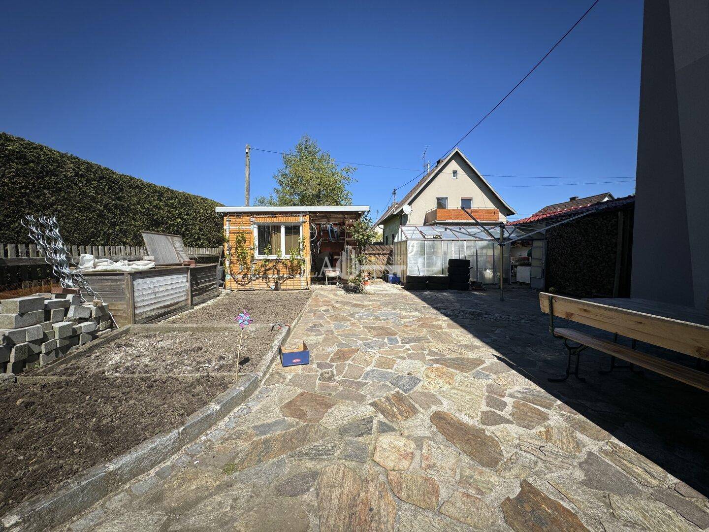 Hinterer Gartenbereich mit Gartenhaus, gepflastertem Weg und Hochbeeten.