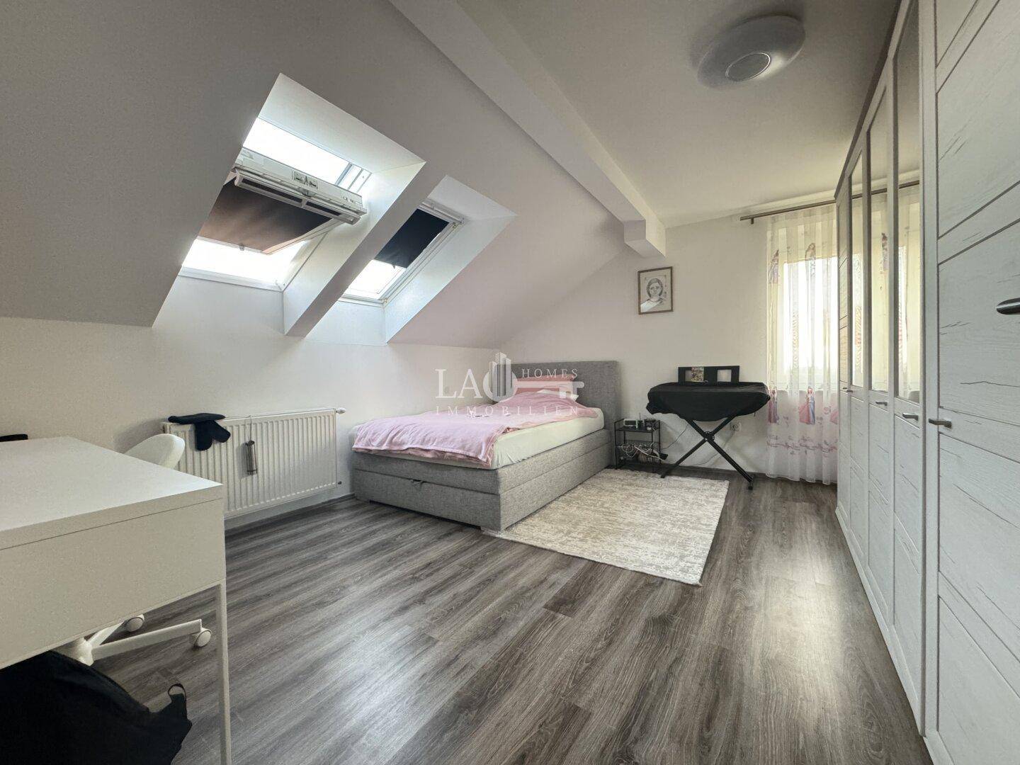 Helles Schlafzimmer im Dachgeschoss mit Bett, Schreibtisch und großen Dachfenstern.