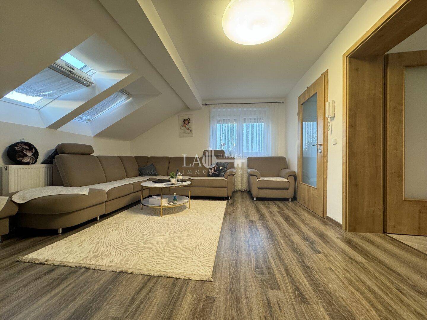 Gemütliches Wohnzimmer im Dachgeschoss mit Laminatboden, Dachfenstern und Ecksofa.