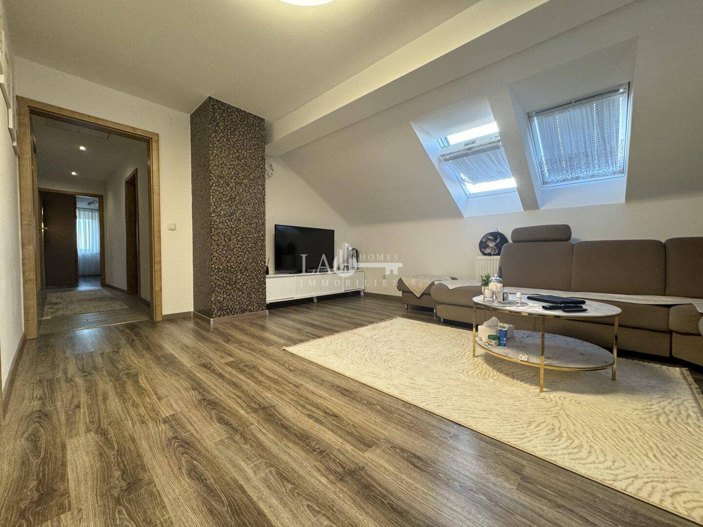 Heller Wohnbereich im Dachgeschoss mit Laminatboden, Fernseher und Dachfenstern.