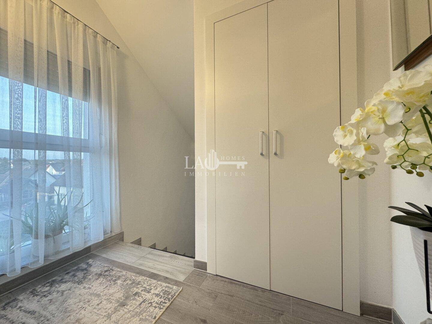 Heller Flur mit Einbauschrank, Fenster und Treppenabgang.