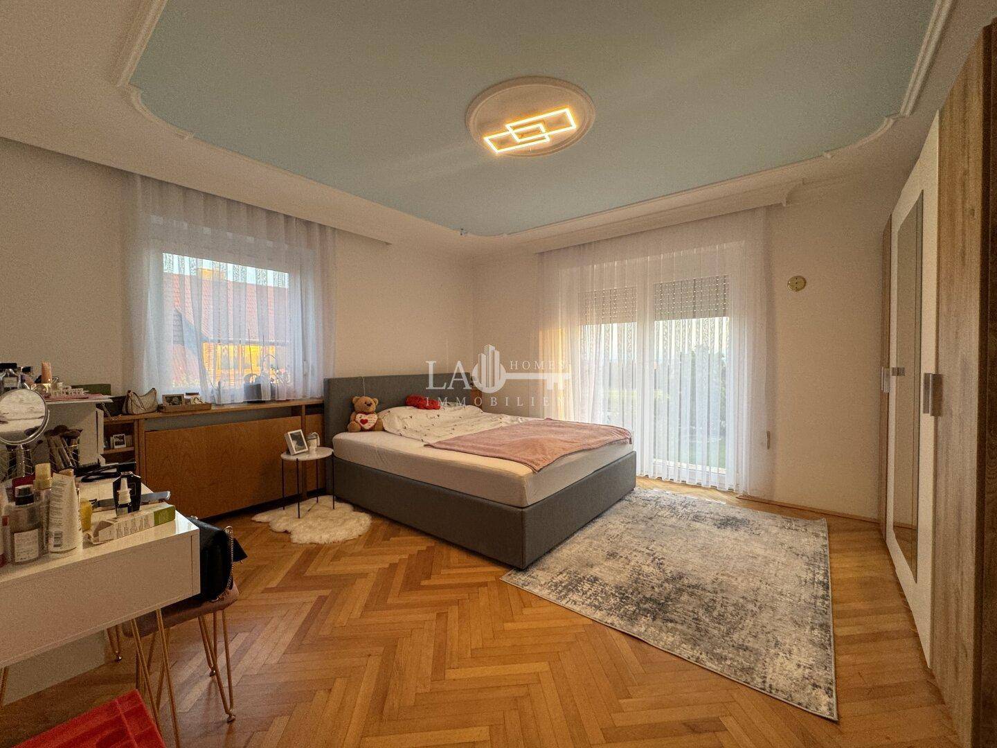 Helles Schlafzimmer mit Parkettboden, Doppelbett und Zugang zum Balkon.