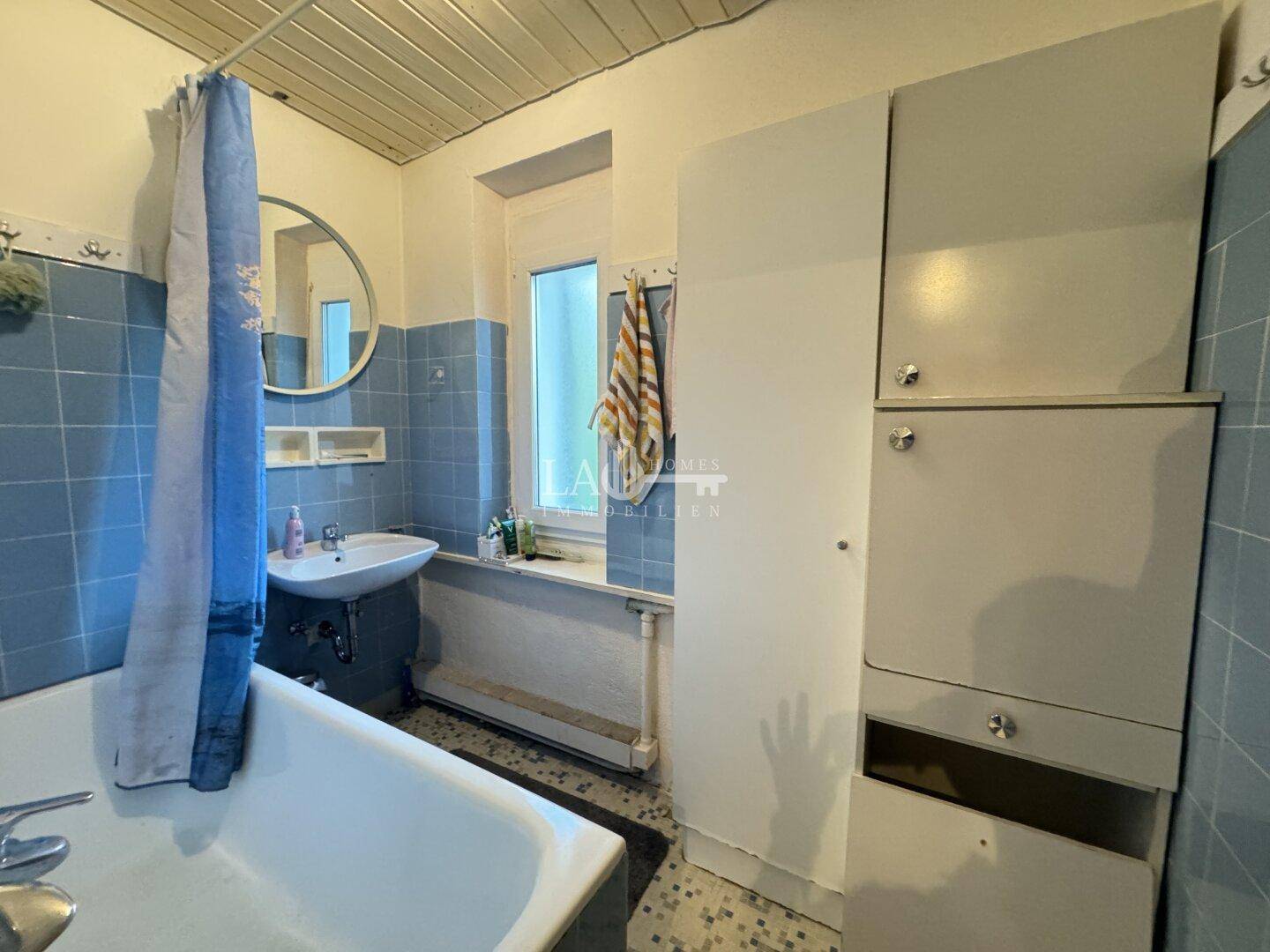 Badezimmer im 80er-Jahre-Stil mit Badewanne, Waschbecken und blauen Fliesen.