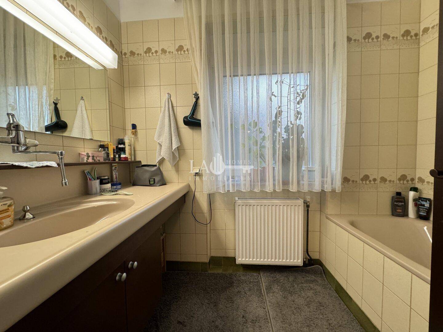 Badezimmer im 80er-Jahre-Stil mit Badewanne, Waschbecken und Fenster.