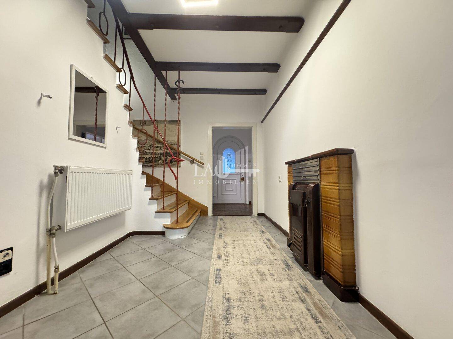 Eingangsbereich mit Treppe, sichtbaren Holzbalken und Fliesenboden.