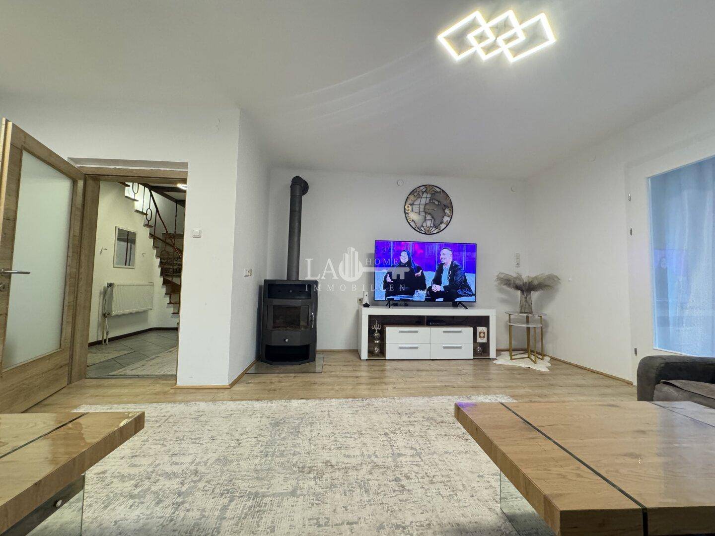 Wohnzimmer mit Kaminofen, Fernseher und Zugang zum Treppenhaus.
