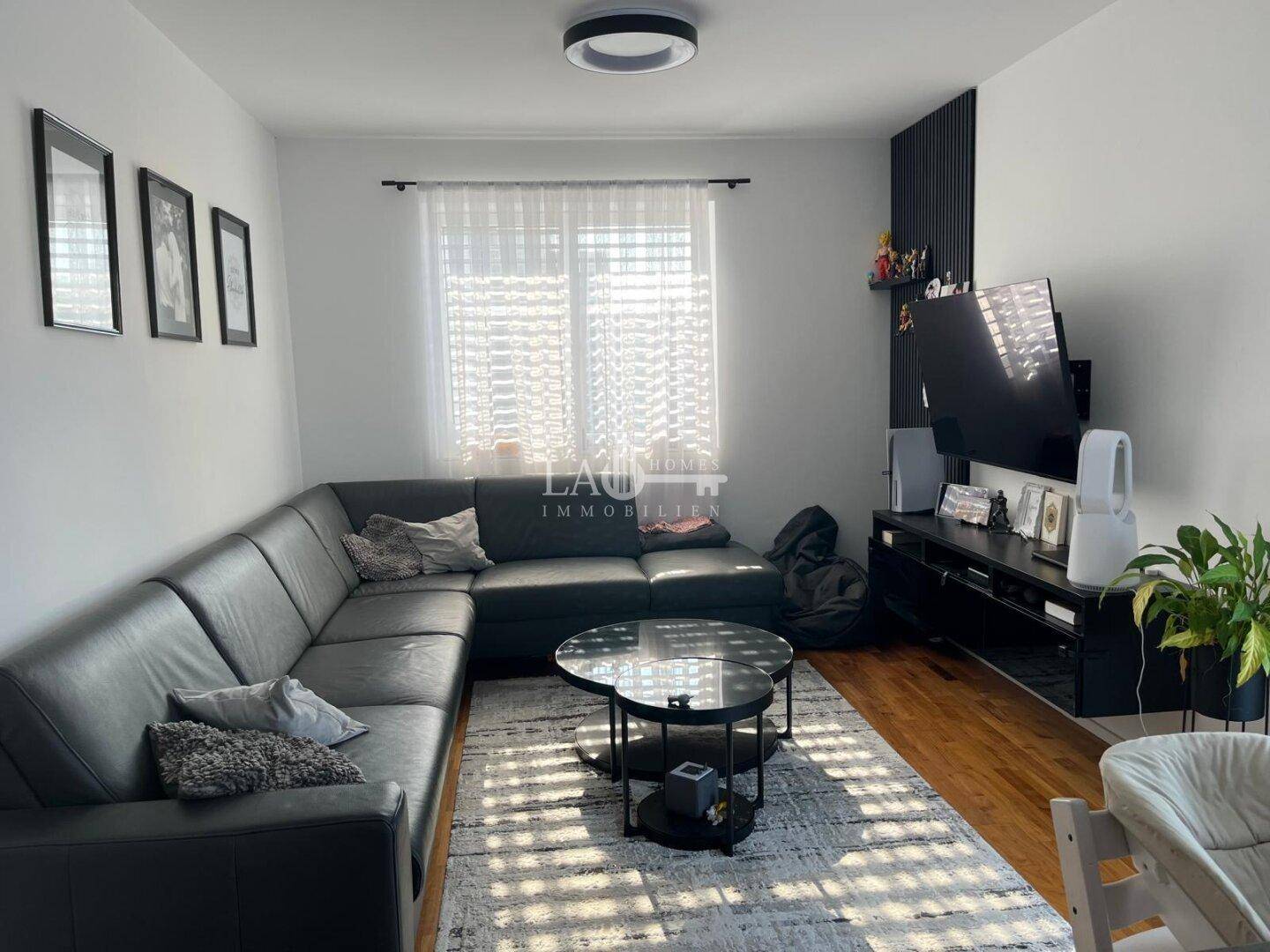 Gemütliches Wohnzimmer mit großem Ecksofa, Holzboden und viel Tageslicht.