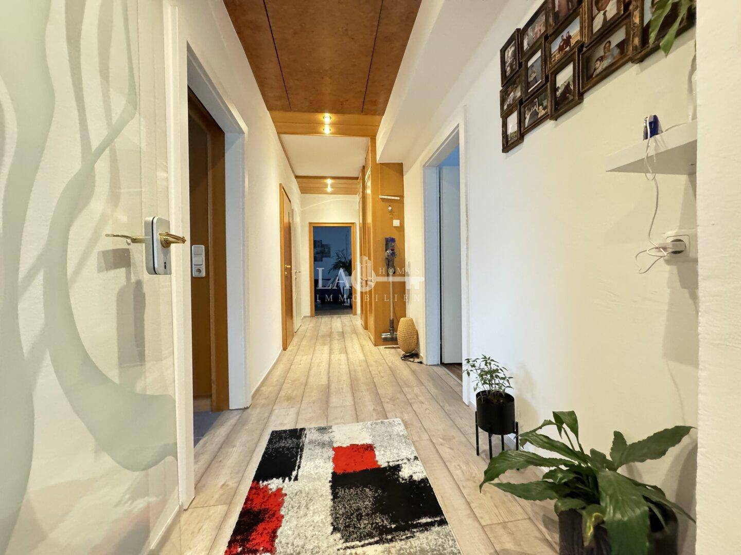 Langer Flur mit hellem Laminatboden, Holzakzenten an der Decke und mehreren Zimmertüren.