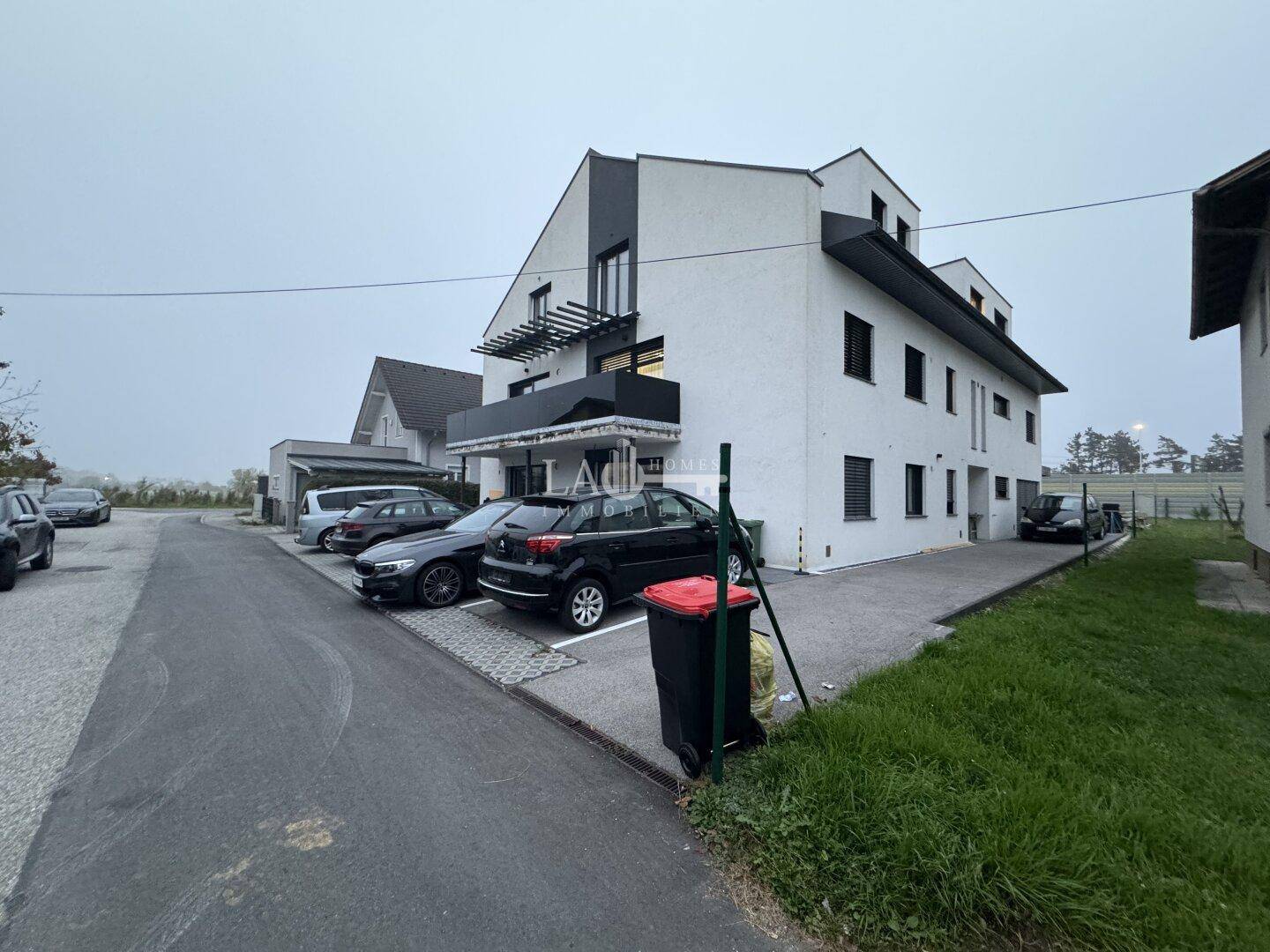 Modernes Mehrfamilienhaus mit weißer Fassade, Balkonen und Außenparkplätzen.