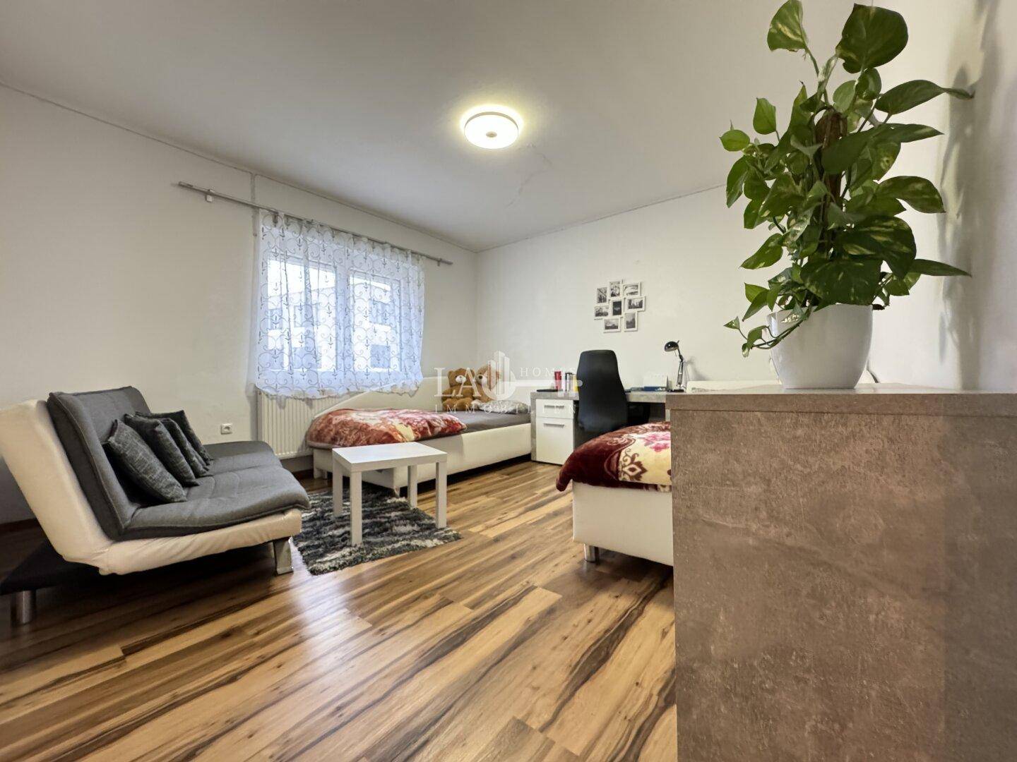 Helles Schlafzimmer mit zwei Betten, einem Schreibtisch und Laminatboden, ideal als Gäste- oder Kinderzimmer.