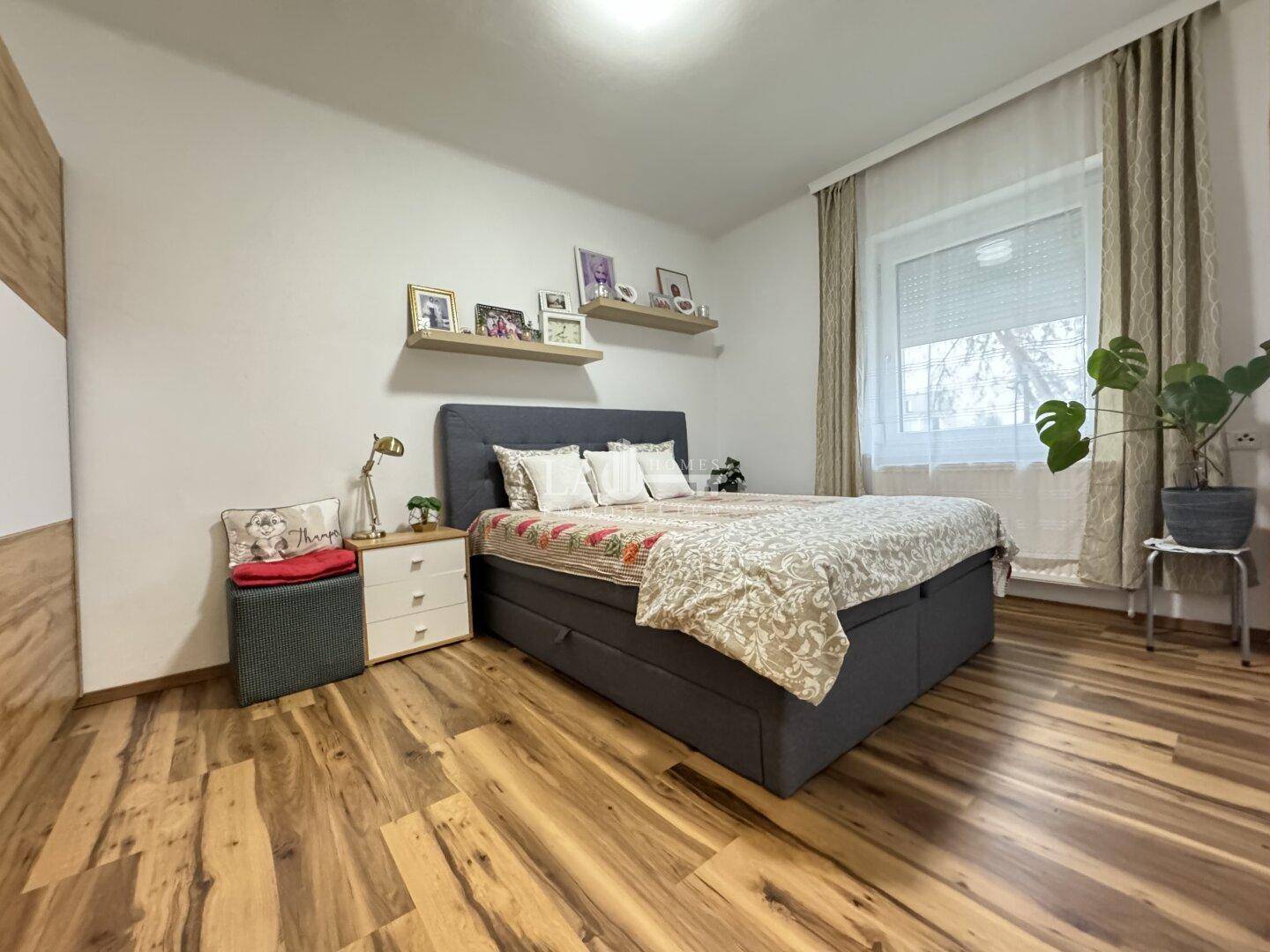 Schlafzimmer mit Doppelbett, Nachttisch und schwebenden Regalen, ausgestattet mit Laminatboden.