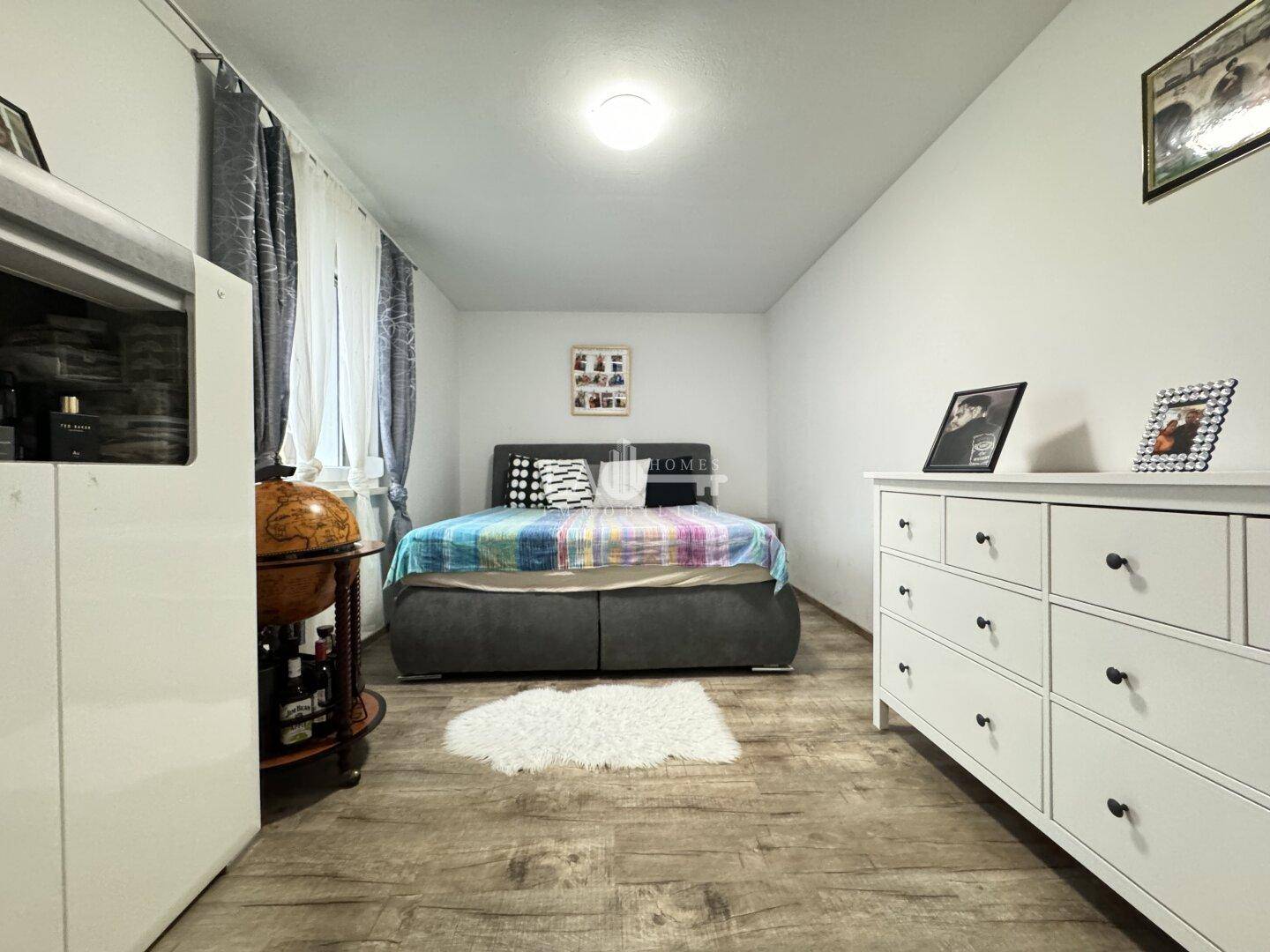 Schlafzimmer mit Bett, weißer Kommode und Laminatboden, bietet ausreichend Stauraum.