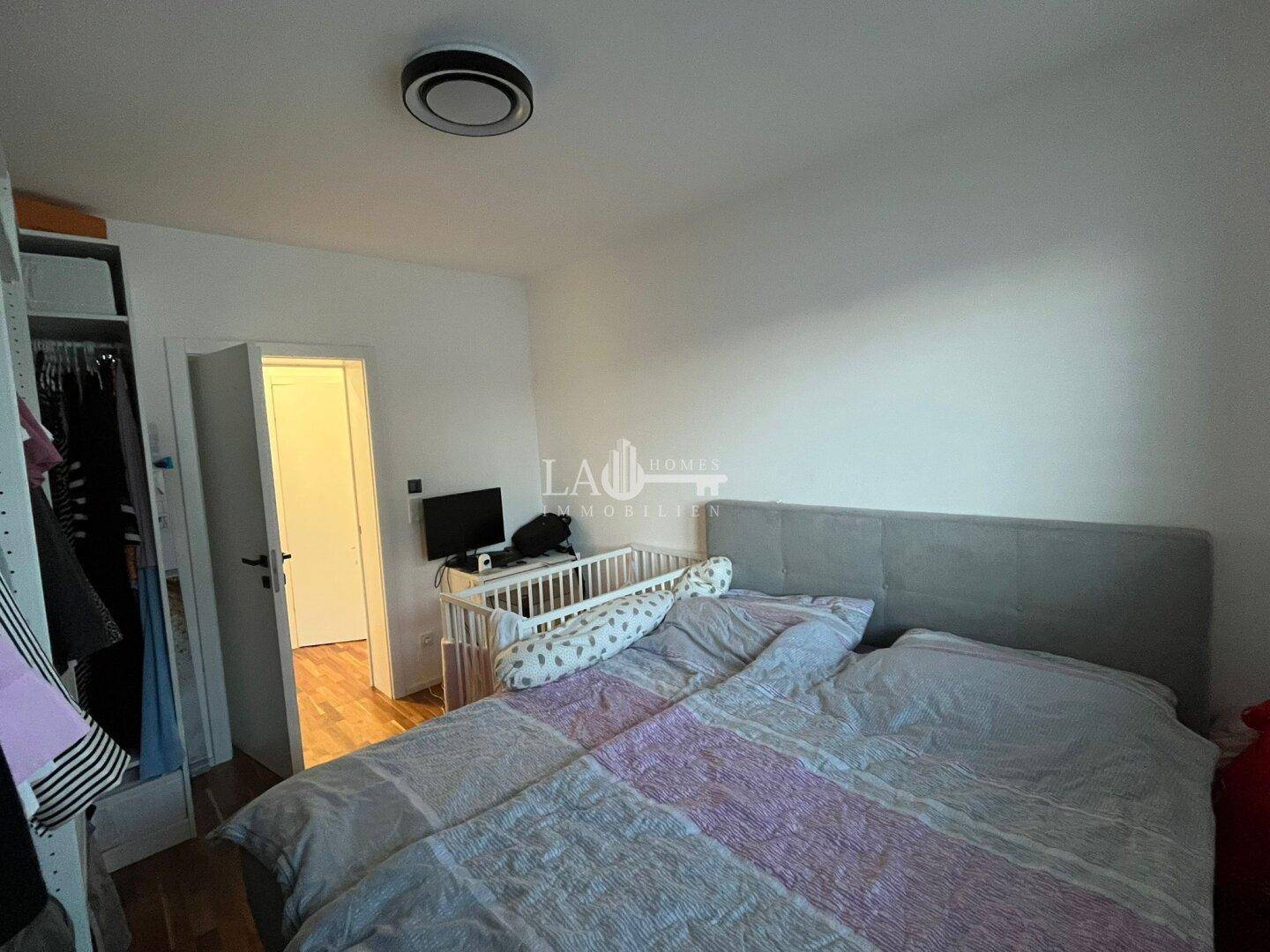 Schlafzimmer mit Doppelbett, Babybett und Zugang zu einem weiteren Raum.