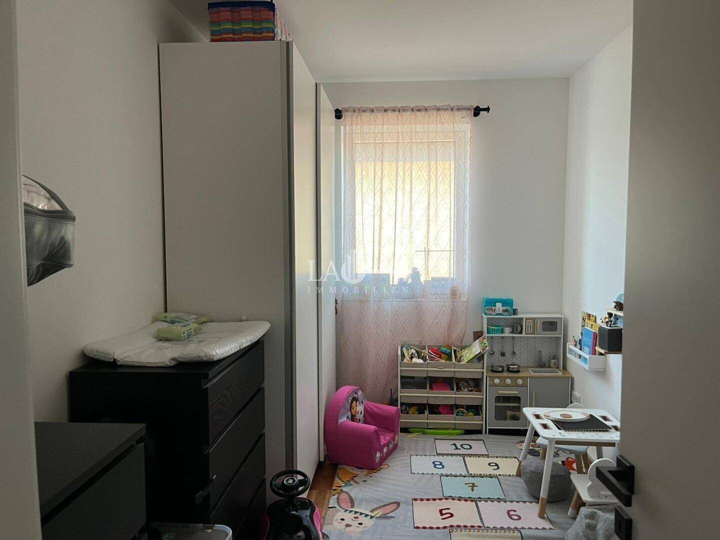 Kinderzimmer mit Spielbereich, Schrank und Fenster für natürliches Licht.