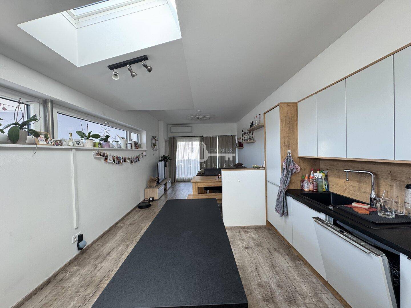 Langer, offener Wohnbereich mit integrierter Küche, Holzboden und Fensterfront für Helligkeit.