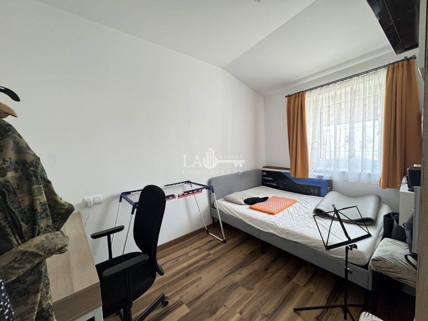 Schlafzimmer mit Holzboden, Fenster und einfacher Einrichtung, ideal als Kinder- oder Gästezimmer.