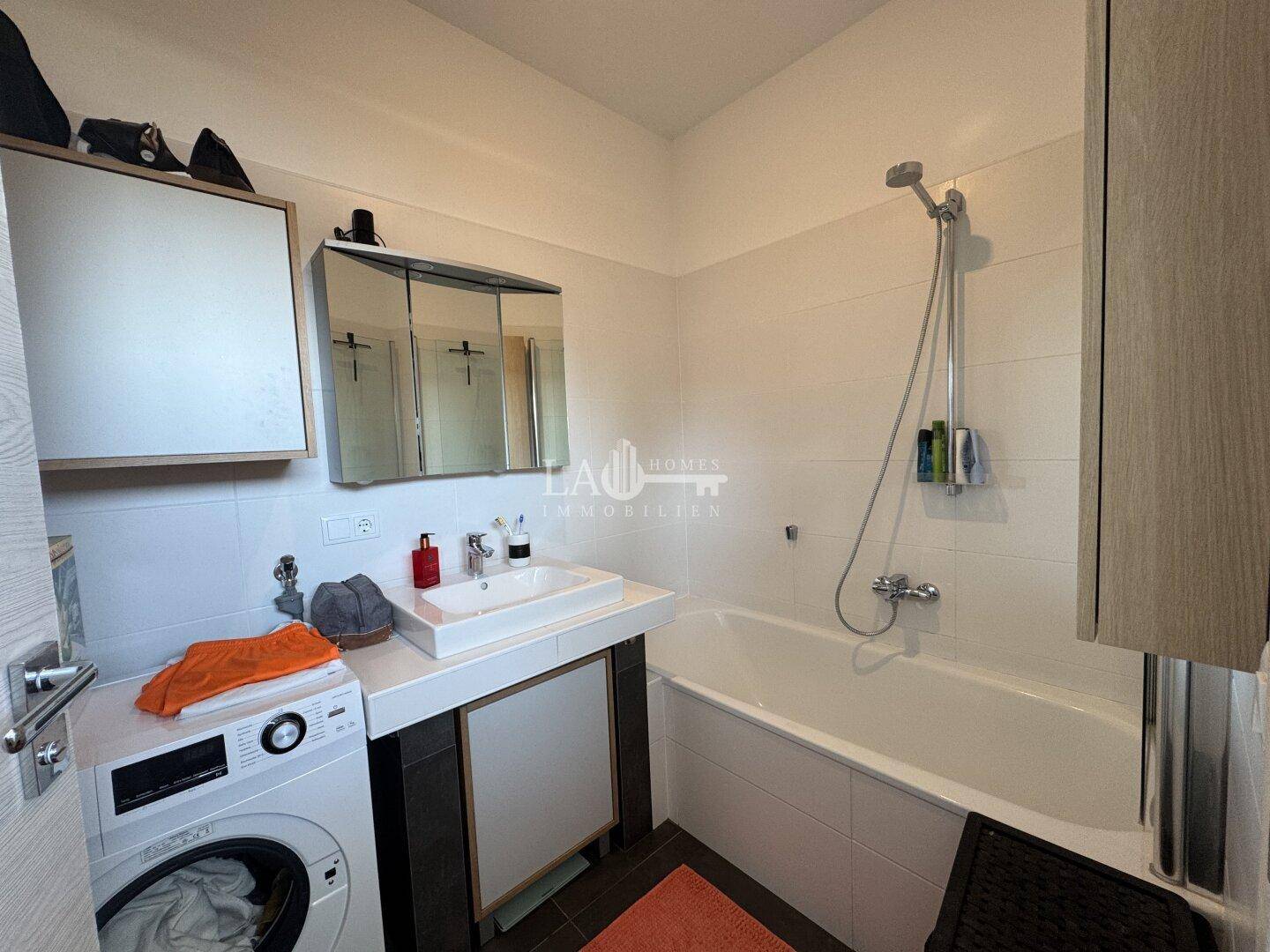 Helles Badezimmer mit Badewanne, Waschbecken und Waschmaschine, funktional und sauber.