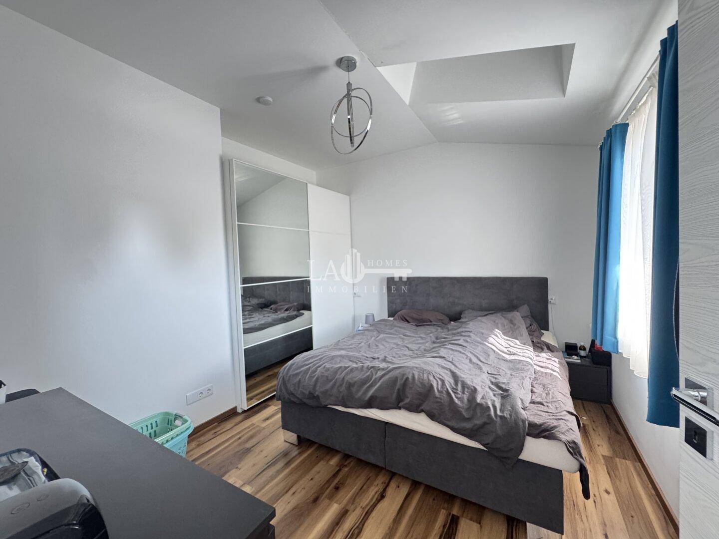 Modernes Schlafzimmer mit Doppelbett, Spiegelschrank und Holzboden, hell und freundlich gestaltet.
