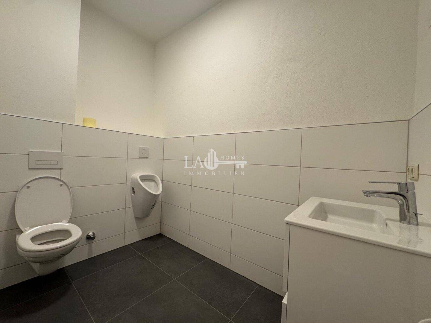 Modernes Gäste-WC mit Wand-WC, Urinal, Waschbecken und weißen Fliesen an den Wänden.