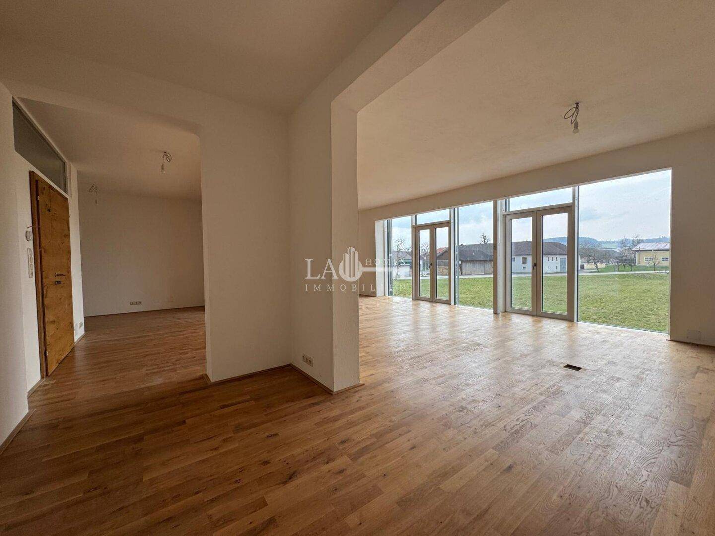 Weitläufiger Wohnbereich mit Holzboden und raumhohen Fenstern, die einen weiten Blick auf die Umgebung ermöglichen.
