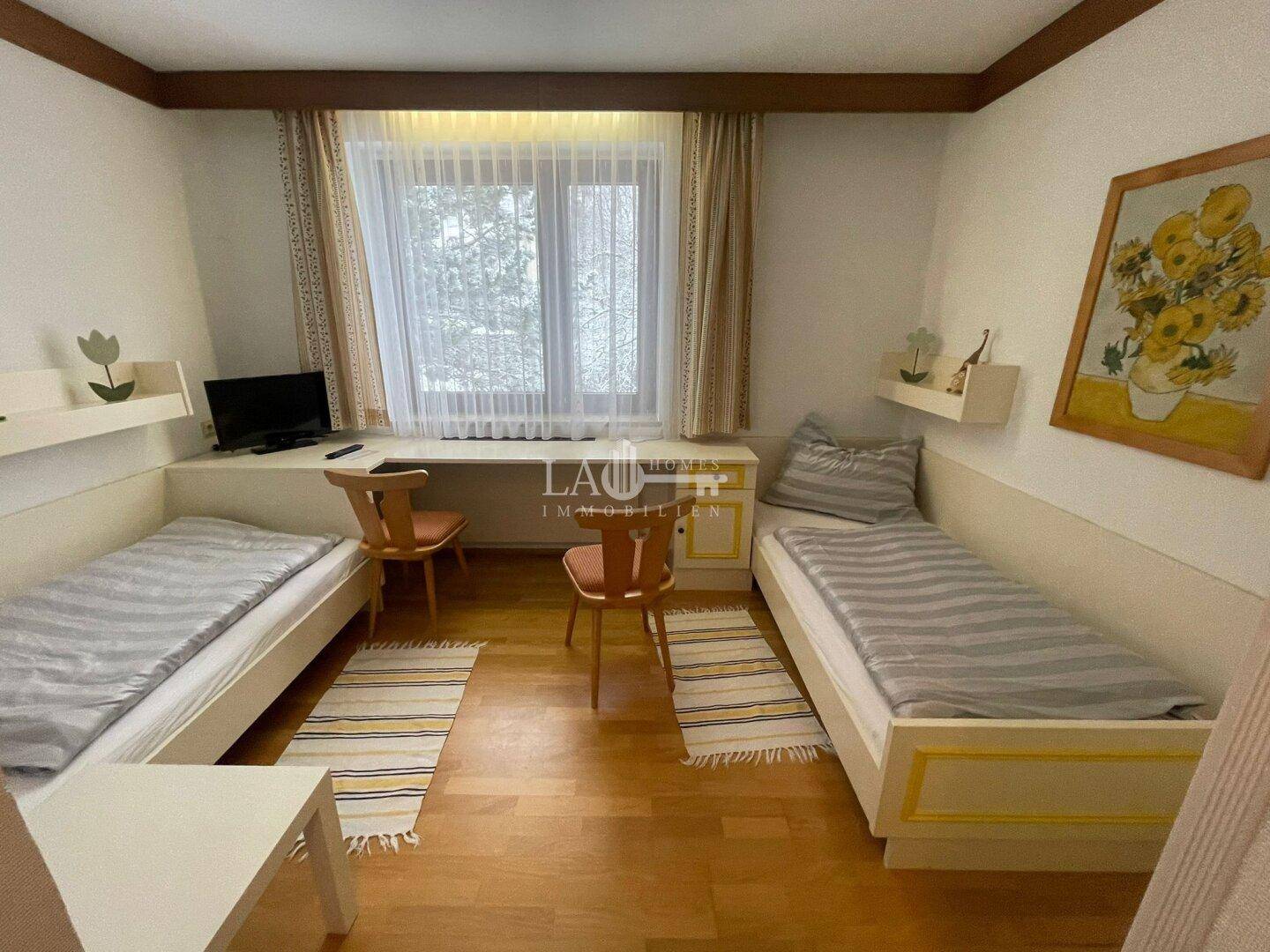 Kinderzimmer mit zwei Einzelbetten, Schreibtisch und einem Fenster mit Blick nach draußen.