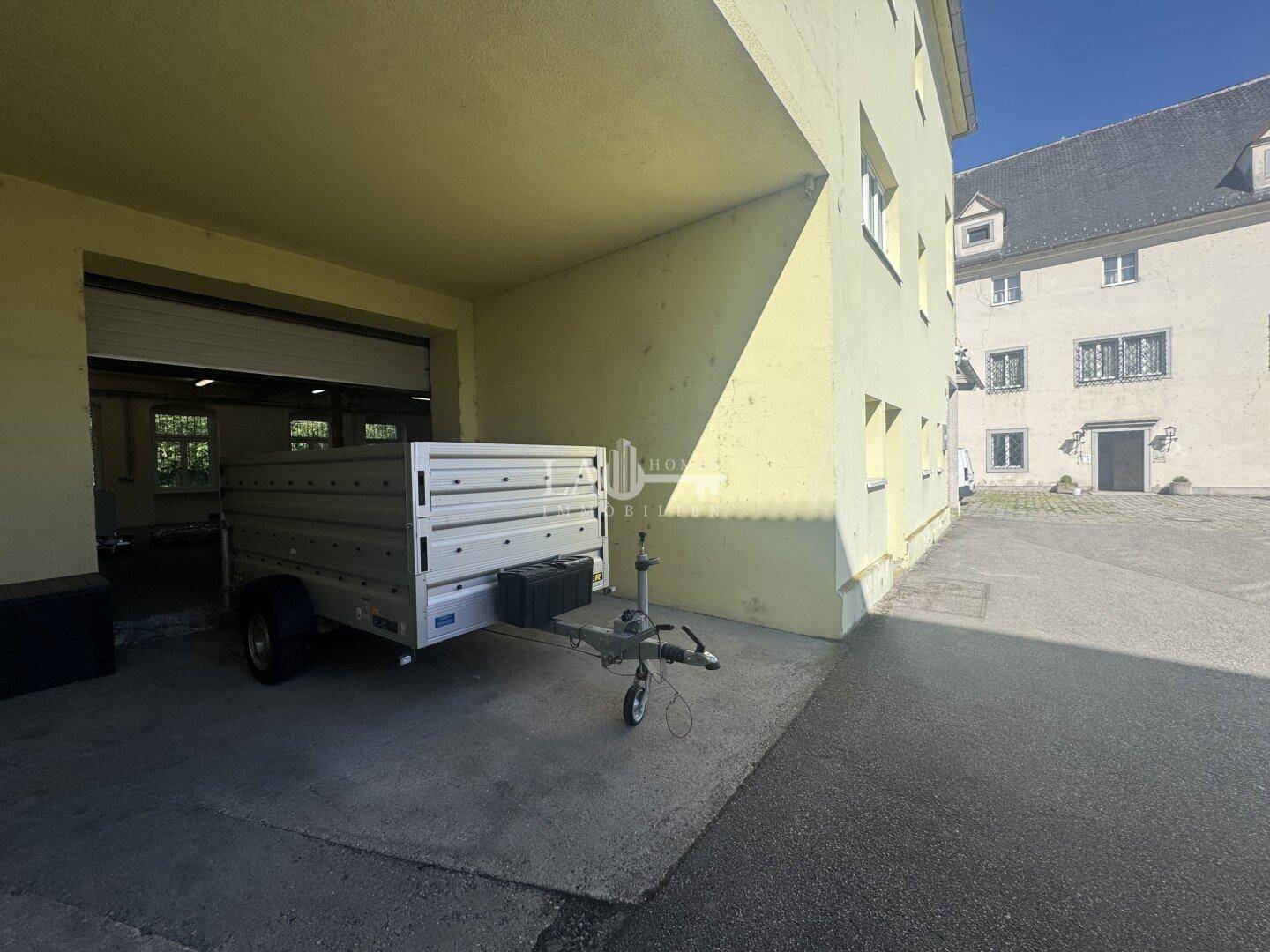 Außenbereich eines Gebäudes mit offener Garageneinfahrt und einem Anhänger unter einem Vordach geparkt.