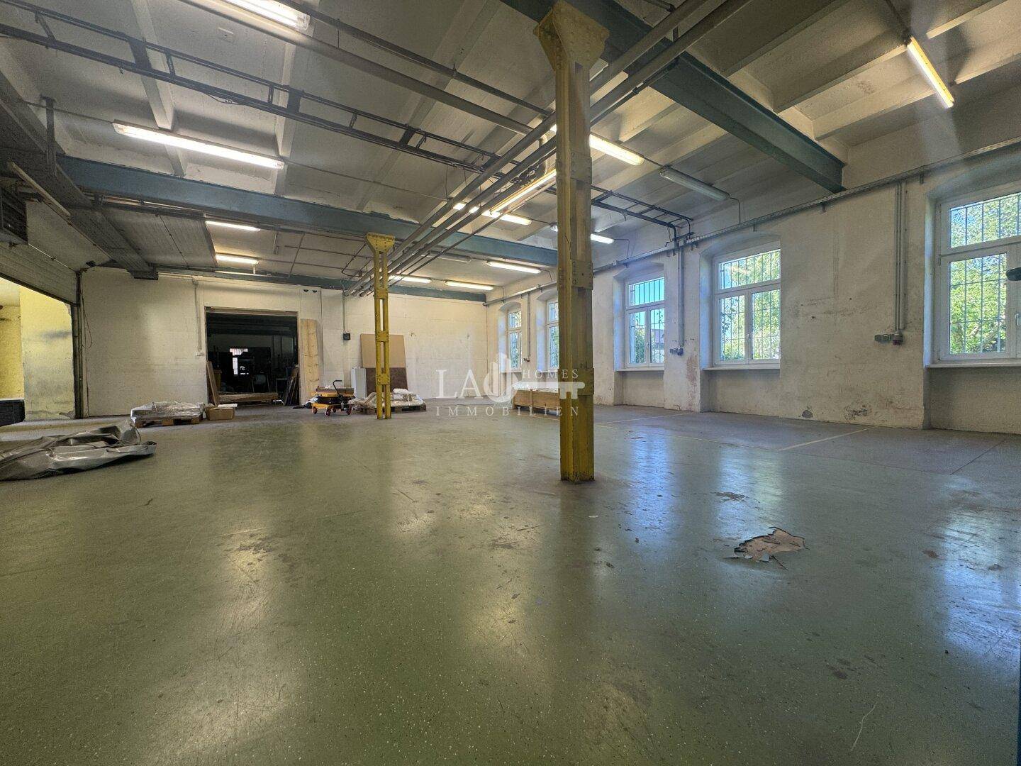 Weitläufige Lagerhalle mit grün gestrichenem Betonboden, hohen Decken und großen Fenstern für viel Licht.