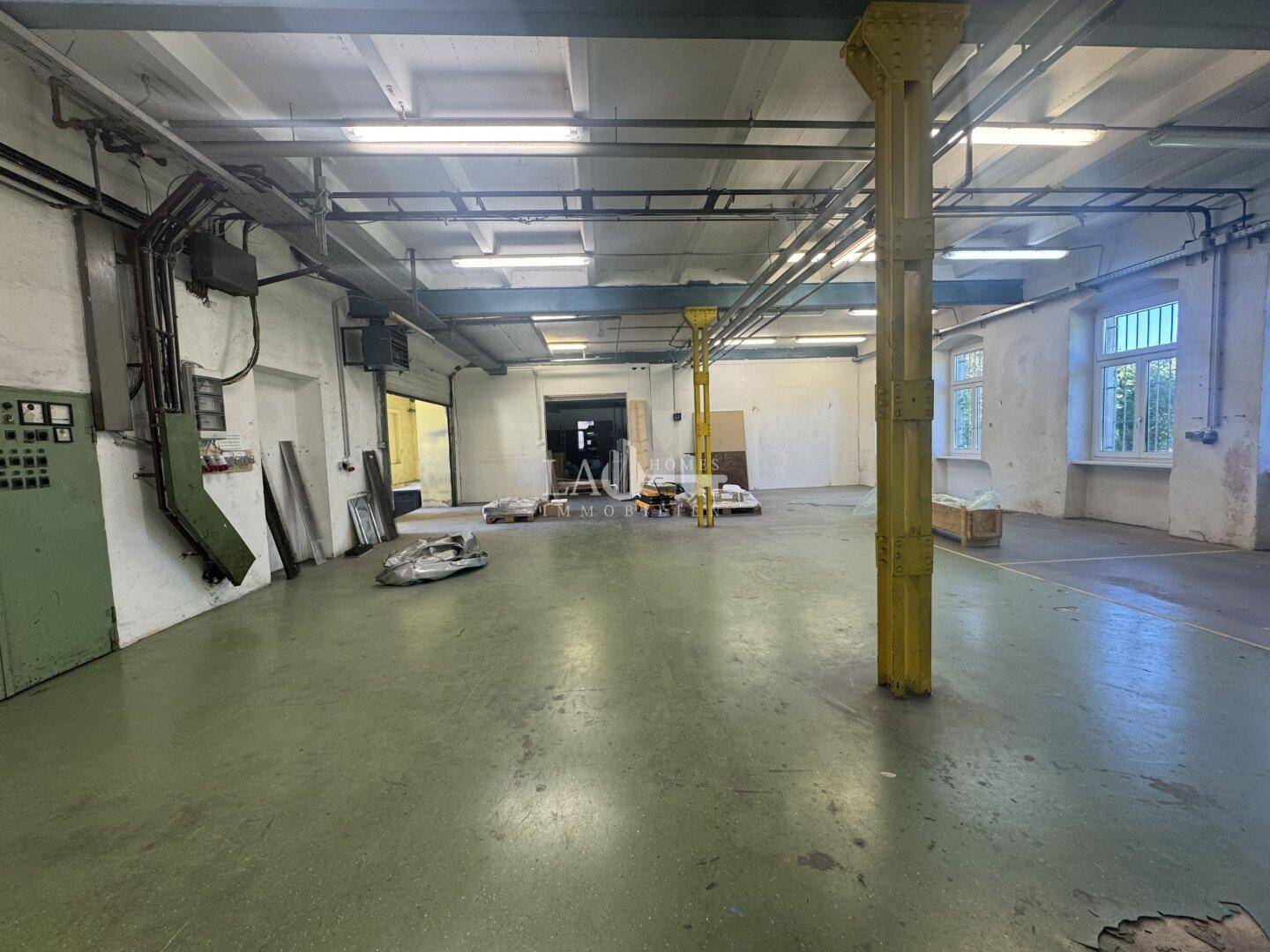 Geräumige Lagerhalle mit grünem Betonboden, gelben Stützpfeilern und sichtbaren elektrischen Installationen.