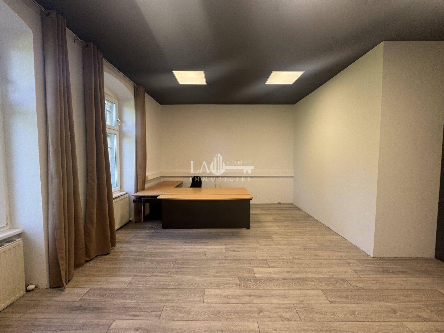 Helles Büro mit Laminatboden, einem modernen Schreibtisch und Vorhängen an den großen Fenstern.