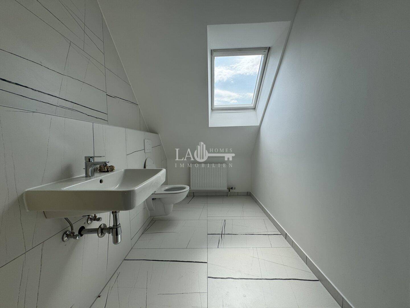 Modernes Badezimmer im Dachgeschoss mit Dachfenster, WC und Waschbecken, hell und funktional.