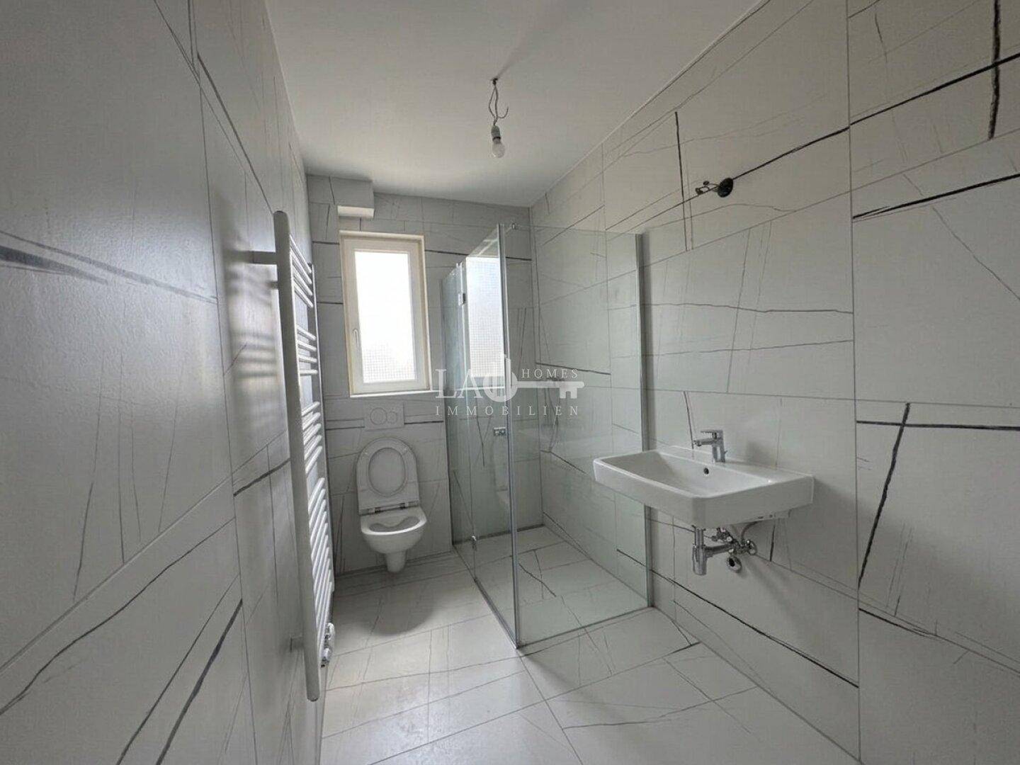 Modernes Badezimmer mit großen Fliesen, ebenerdiger Dusche, Wand-WC und Handtuchheizkörper.
