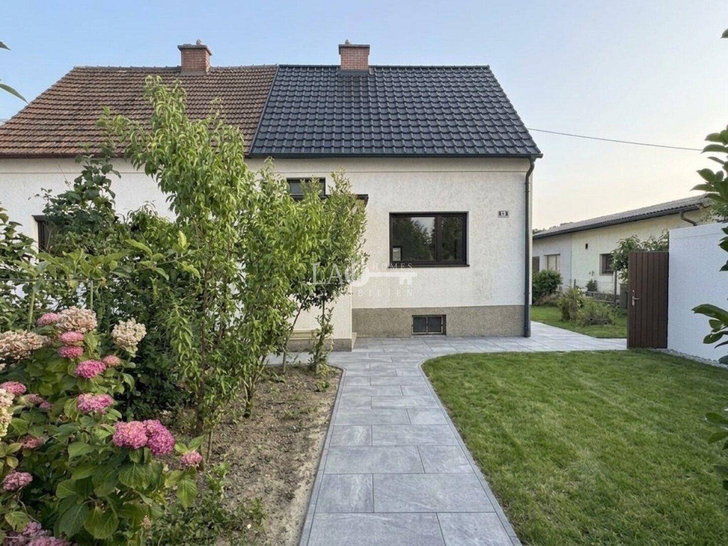 Seitenansicht eines Hauses mit neu gepflastertem Weg und gepflegtem Vorgarten.