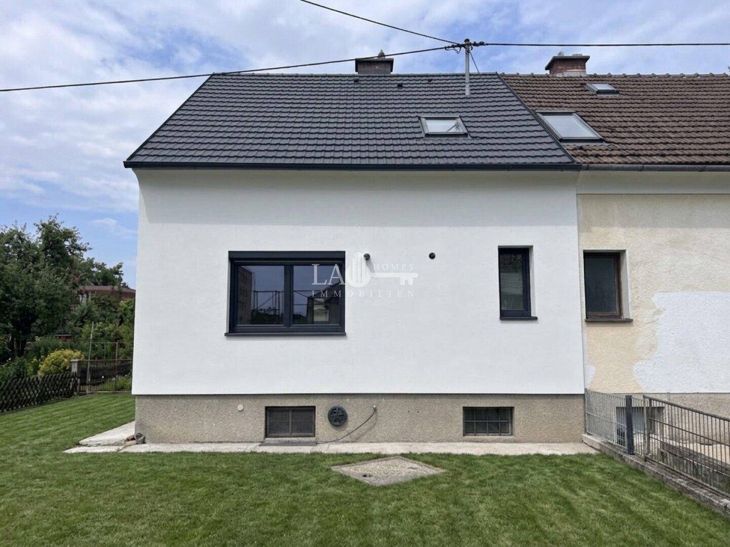 Rückansicht des Hauses mit weißer Fassade, neuen Fenstern und grünem Rasen.