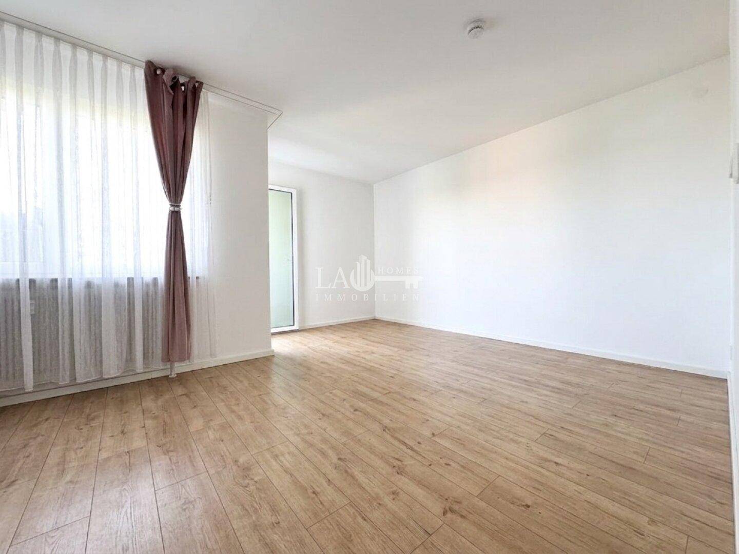 Heller Wohnbereich mit Laminatboden und viel Tageslicht durch das große Fenster.